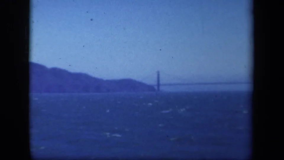 Wide 8mm view of San Francisco Bay and the distant Golden Gate Bridge, framed by dark borders and strong blue film color.