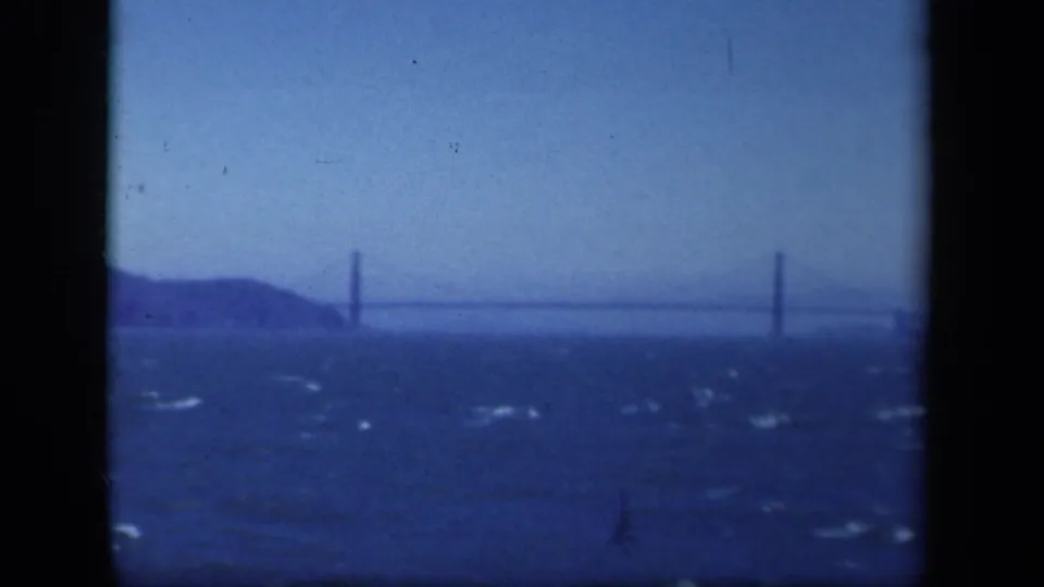 1941 New York-area 8mm frame showing a distant suspension bridge beyond dark, wind-ruffled water and a low shoreline.