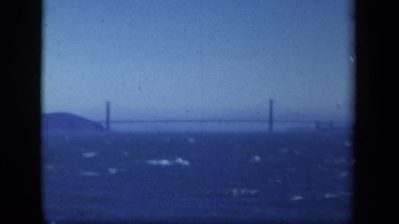 Suspension bridge and shoreline seen through dark film-frame borders.
