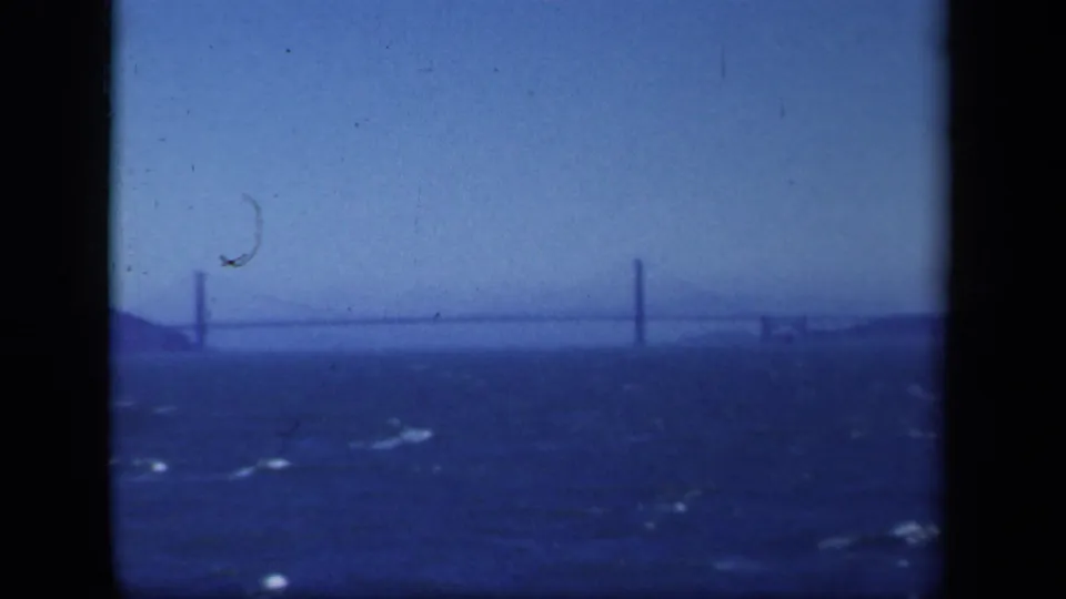 1941 New York-area 8mm frame showing a distant suspension bridge, textured water, hazy horizon, and visible film wear.