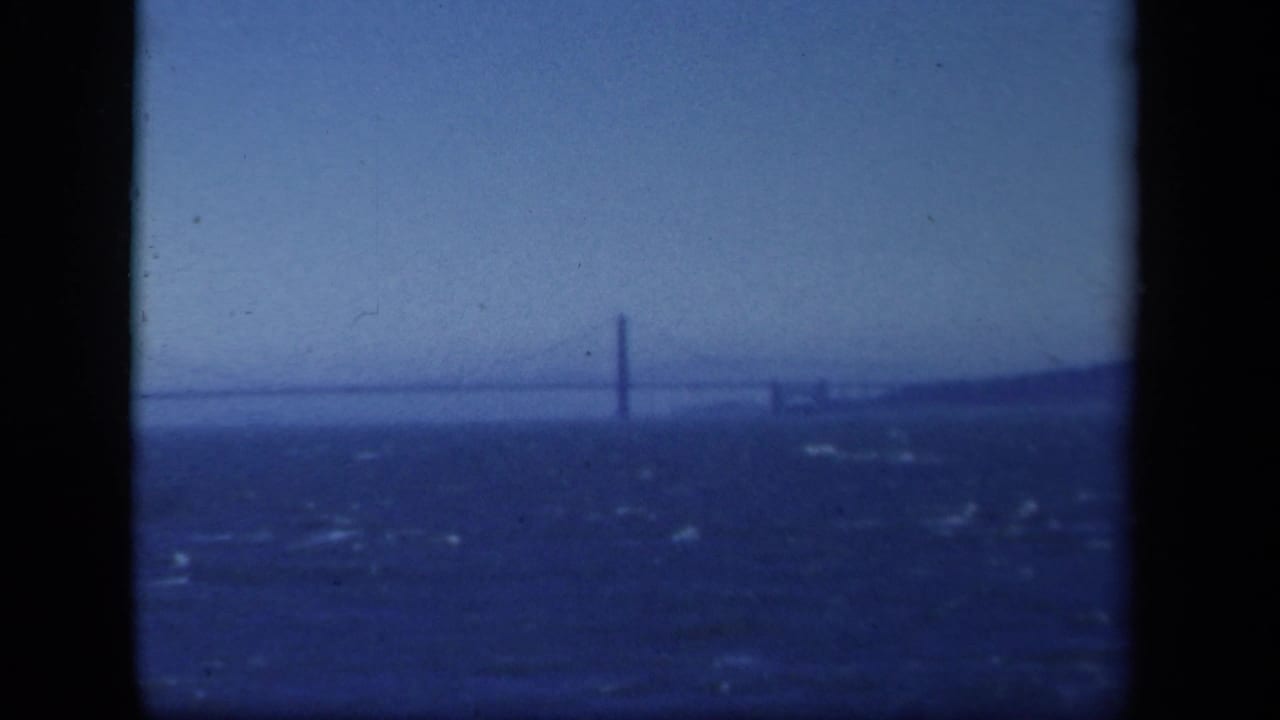 Distant suspension bridge over choppy water with hazy sky and dark film borders.
