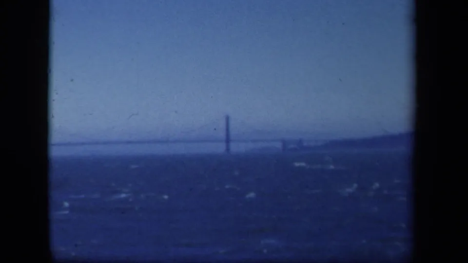 1941 New York 8mm frame showing a distant suspension bridge across choppy water under a hazy blue sky.