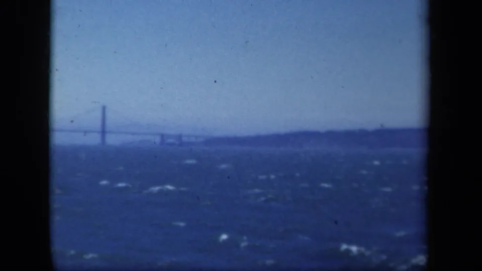 1941 New York home-movie frame with a distant suspension bridge, low landmass, and textured waves in the foreground.