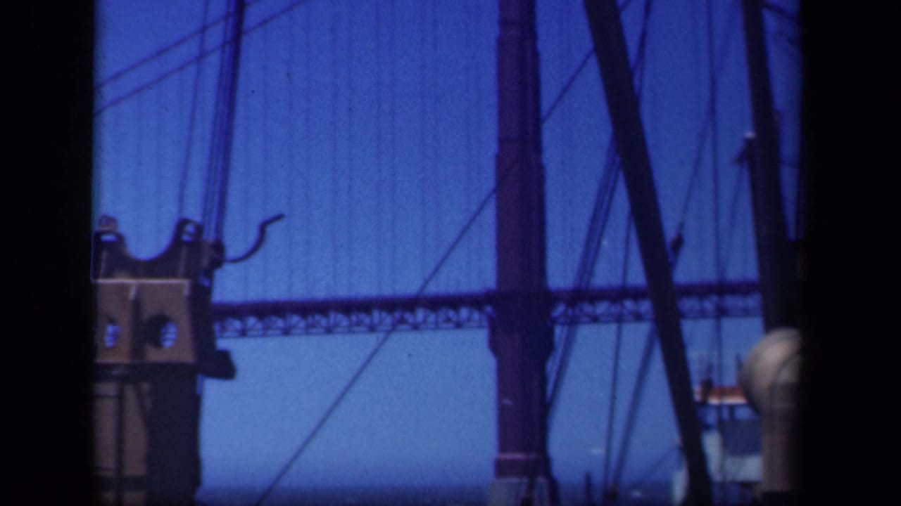 Close view of a large suspension bridge tower and cables, partly obscured by boat rigging in 8mm footage.