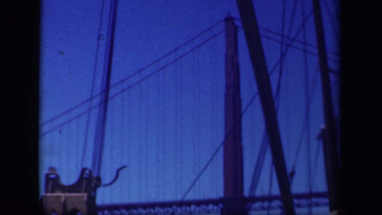 1941 8mm frame showing a large suspension bridge with towers and cables, viewed through dark gate edges in blue-tinted color.
