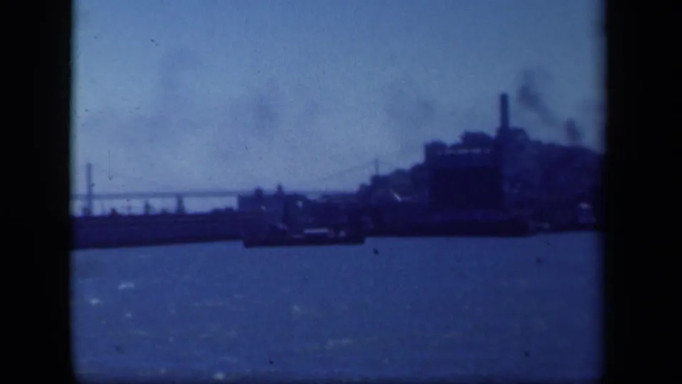 1941 New York metadata frame showing a distant industrial shoreline across water, with a bridge span at left and smoke rising from buildings.