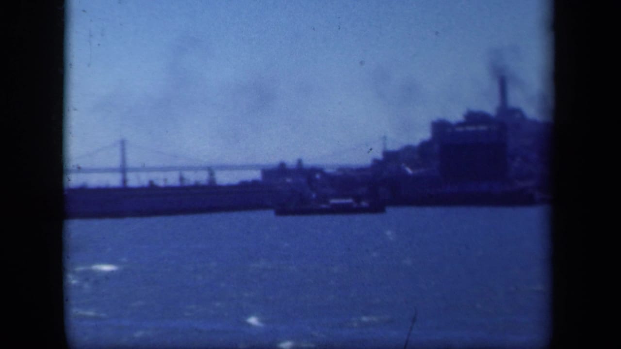 1941 New York-area 8mm frame showing a soft blue harbor panorama with bridge spans, waterfront structures, and a low vessel shape.
