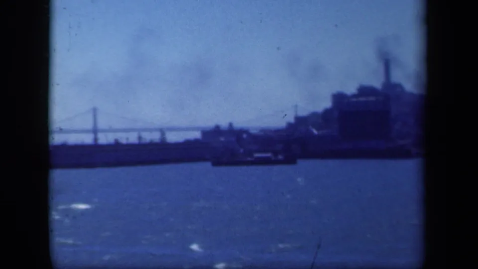 1941 New York-area 8mm frame showing a soft blue harbor panorama with bridge spans, waterfront structures, and a low vessel shape.