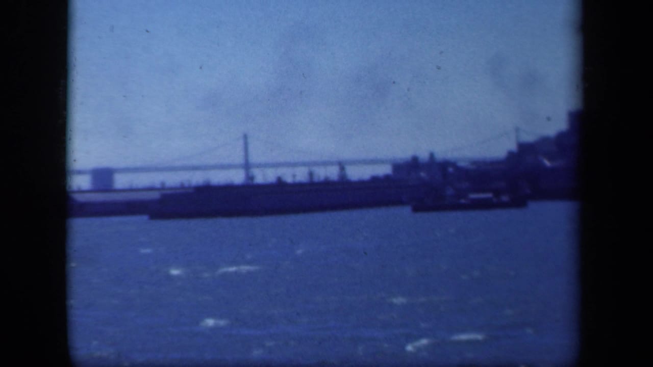 Suspension bridge spans a blue body of water with a dark shoreline form in the foreground.