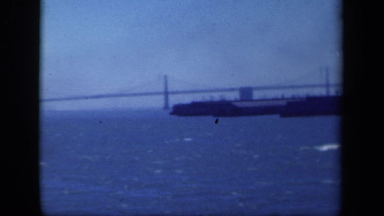 Distant suspension bridge over water with a large vessel in the foreground.