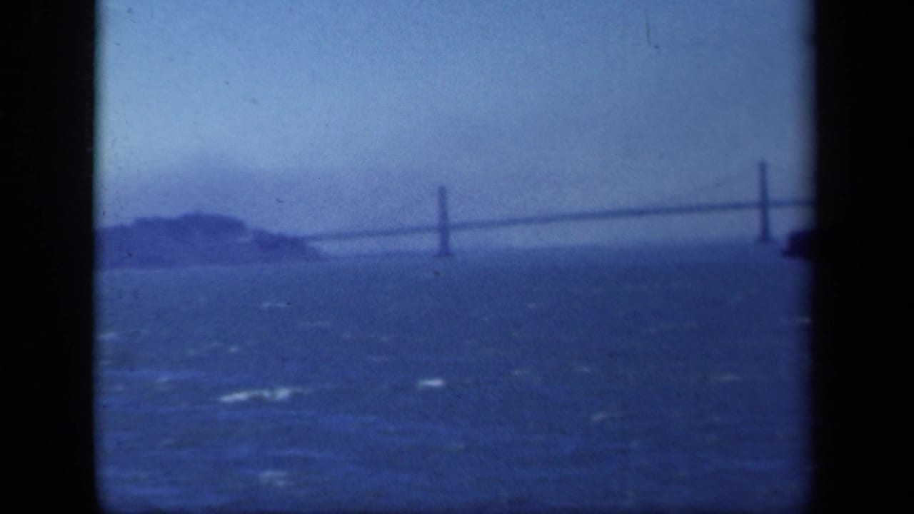 Soft blue view across choppy water toward a long suspension bridge and distant island.