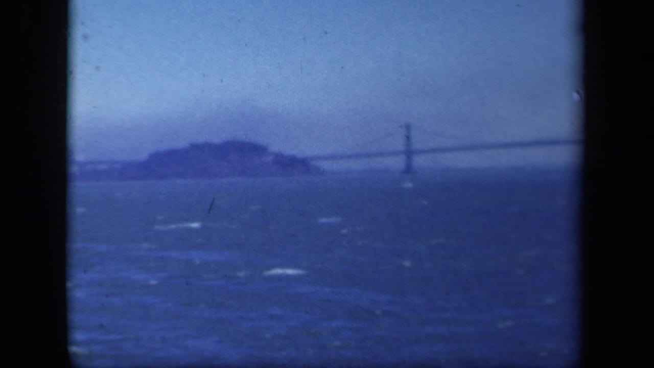 Distant island and suspension bridge seen across dark blue water with whitecaps.