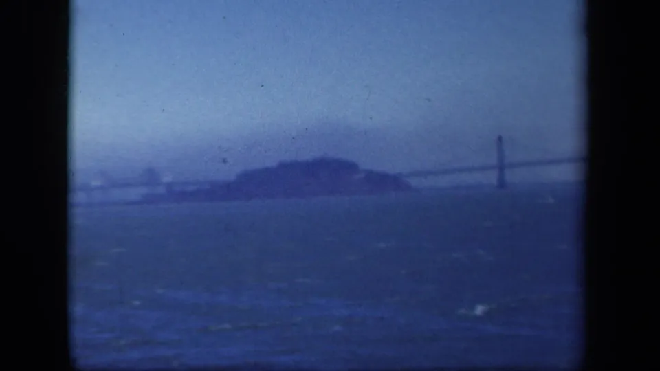 Final 1941 8mm frame with rough blue water, an island silhouette, and a suspension bridge tower and span fading into haze.