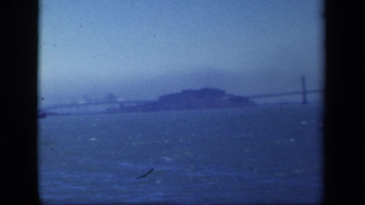 Distant island and bridge seen across blue bay water through dark film borders.