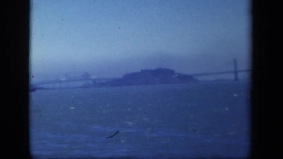 1941 home-movie frame showing a hazy distant view of San Francisco Bay landmarks across choppy blue water.