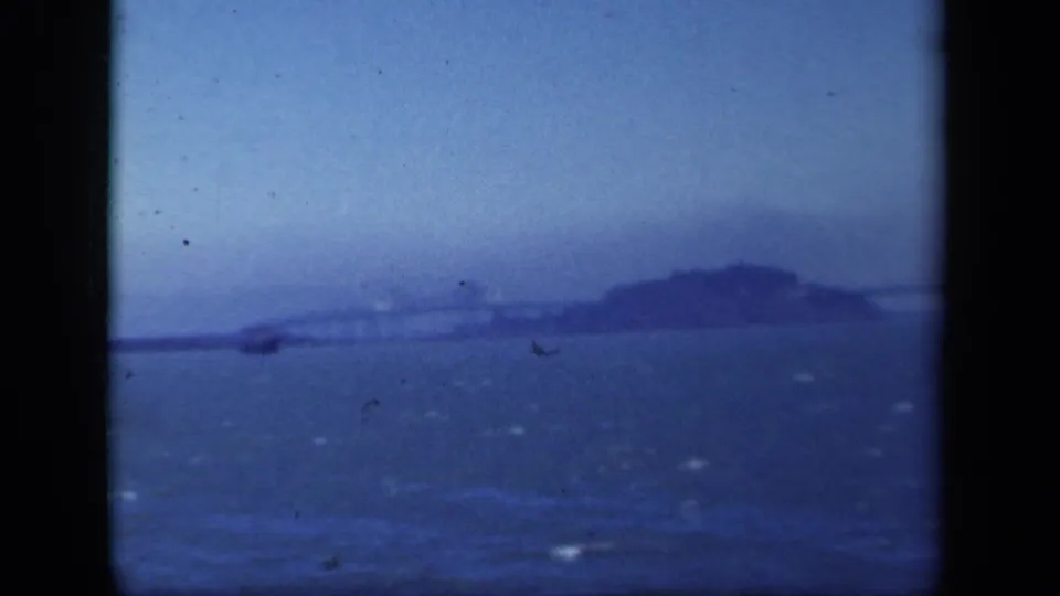 1941 color 8mm frame with a small boat crossing the foreground below the distant Bay Bridge area and island silhouette.