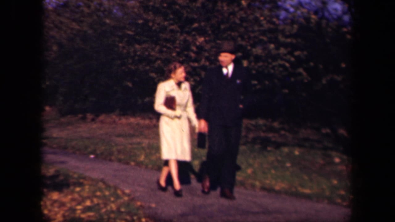 Two adults walk together on a paved park path bordered by grass and trees.