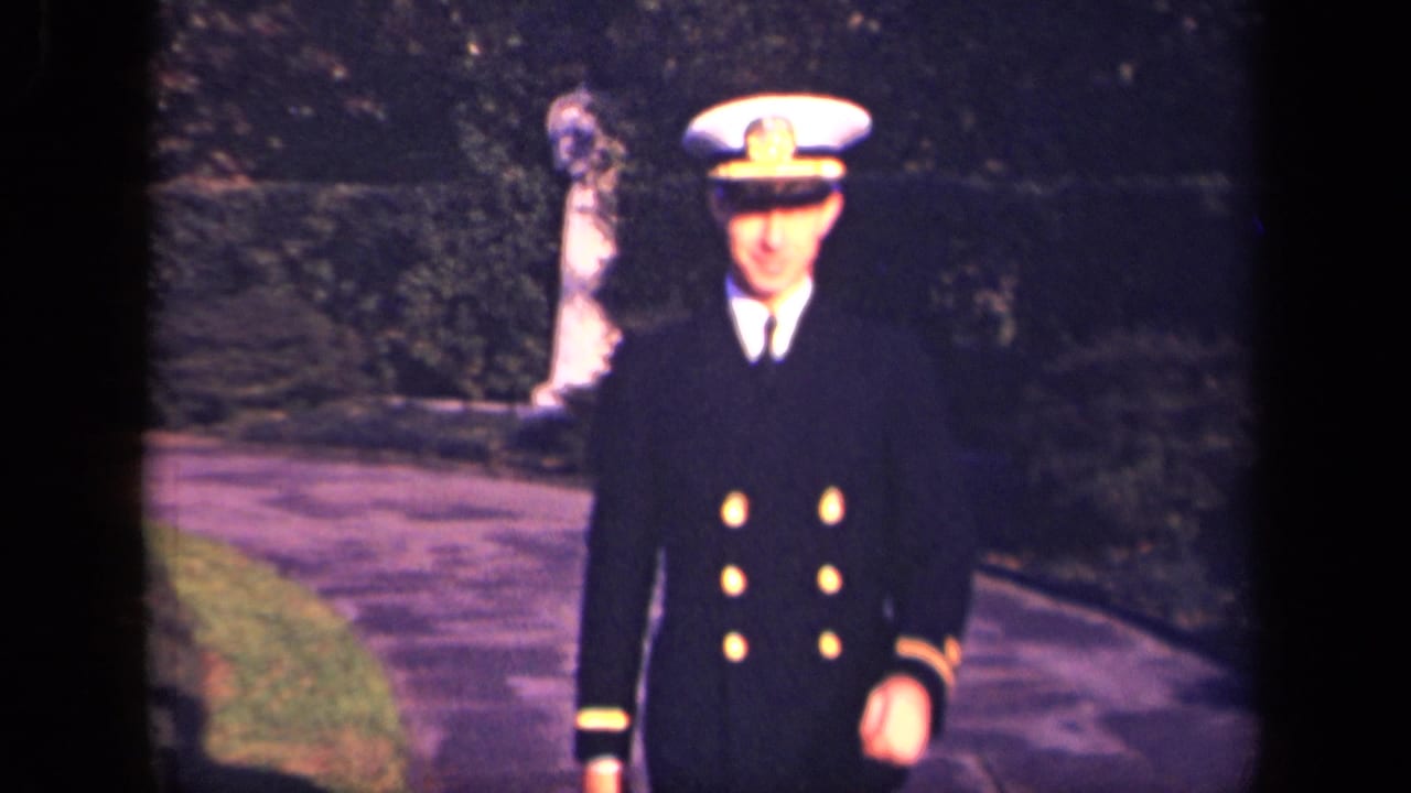 The officer walks nearer in the New York garden setting, his white cap and dark naval jacket prominent.