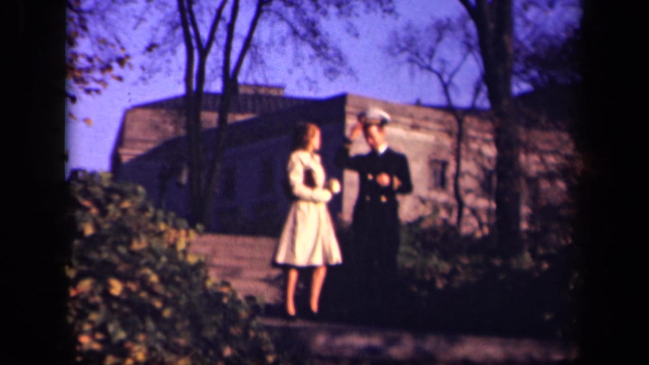Young woman in a light dress stands with a uniformed man near a stone building.