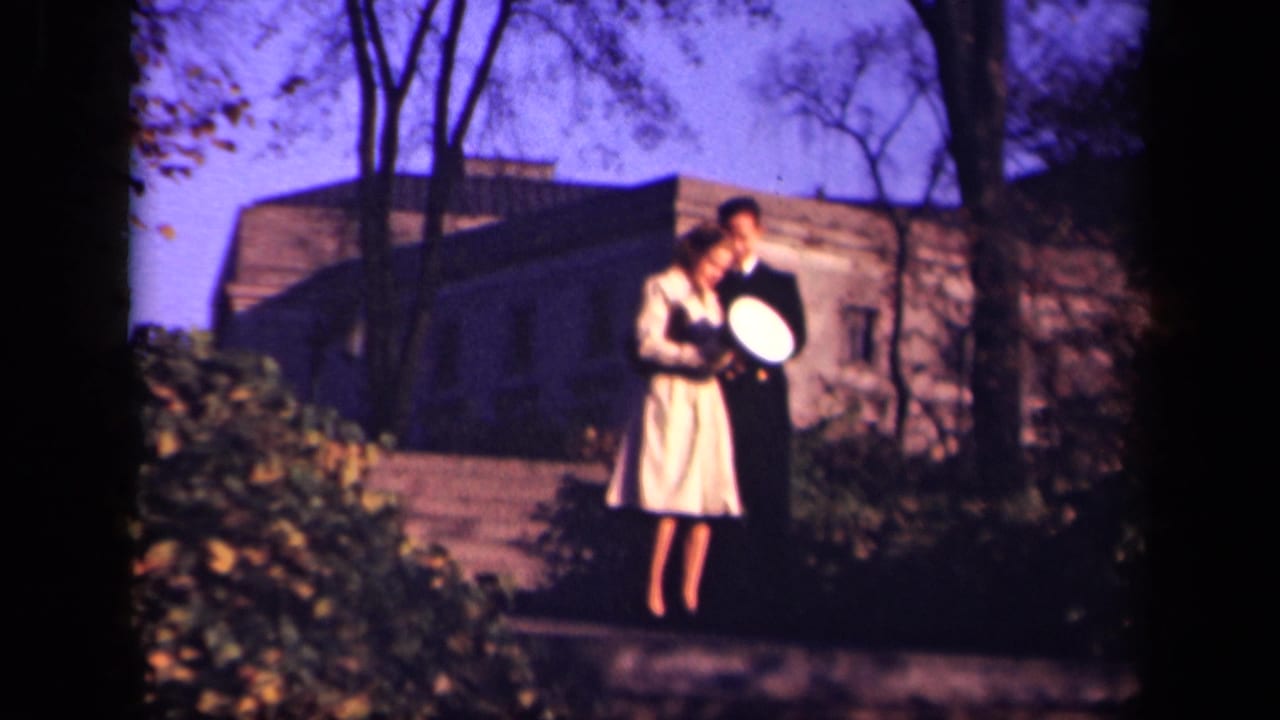 Uniformed man shows a light-colored hat to a young woman on an outdoor path.