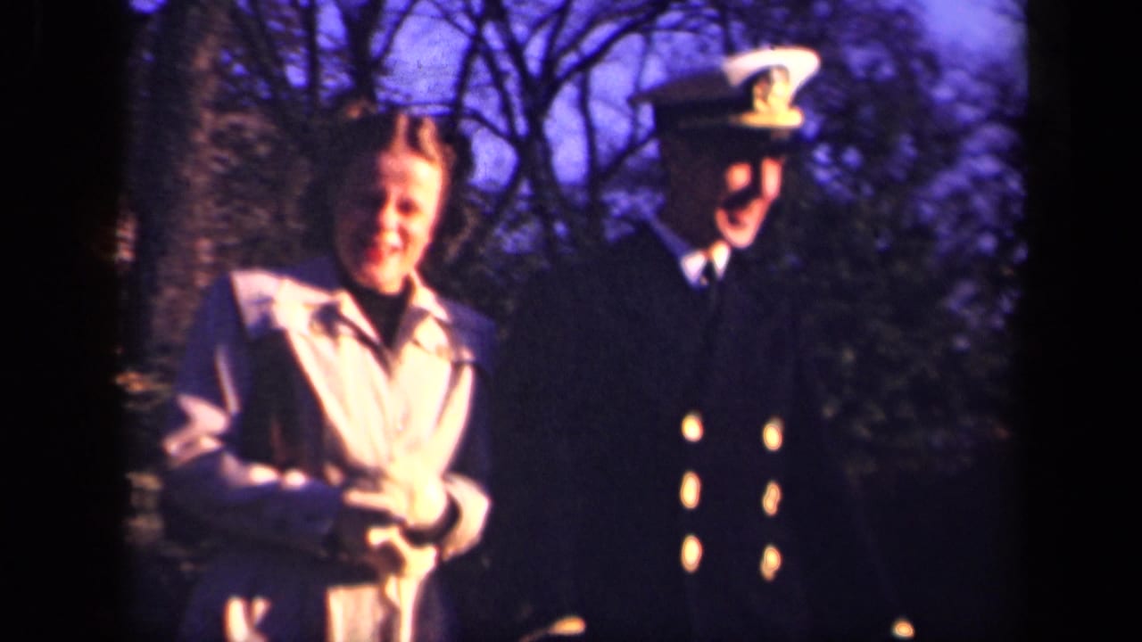 Smiling woman stands near a man in naval uniform holding a white cap.