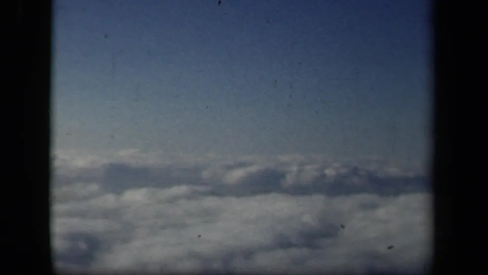 The final frame continues the airplane-window view, showing cloud cover below and open blue sky above with dark framing at the edges.