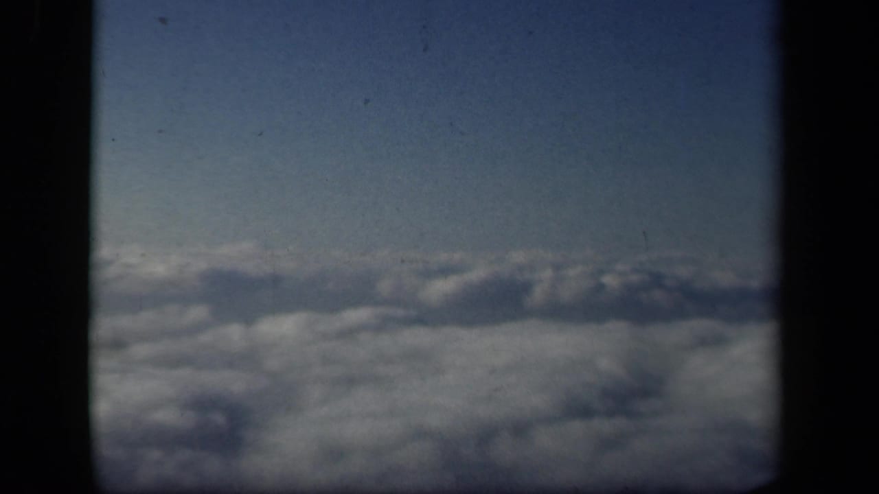 Aerial clouds and blue sky divided by a dark vertical aircraft window bar.