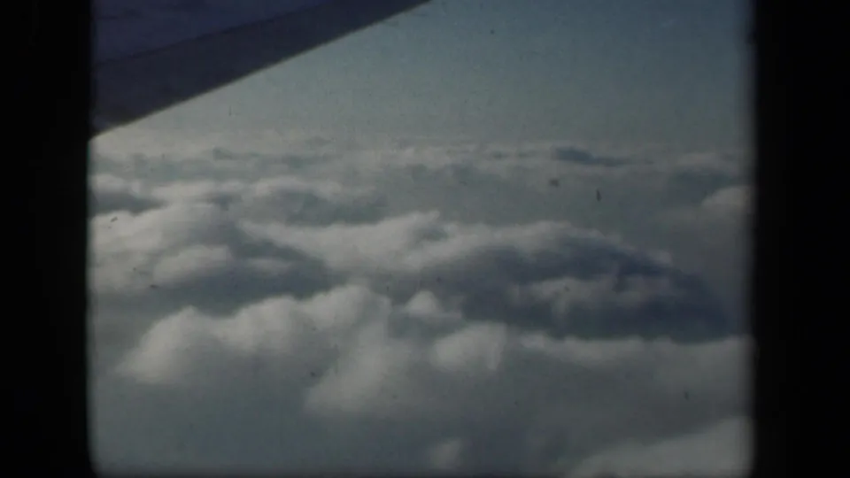 Aerial view from a 1941 8mm flight, with clouds below and a dark airplane wing edge crossing the upper frame.