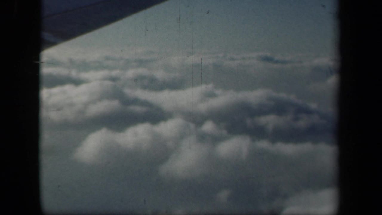 1941 8mm home-movie frame showing clouds from an airplane window, with the aircraft wing corner and dark frame edges visible.
