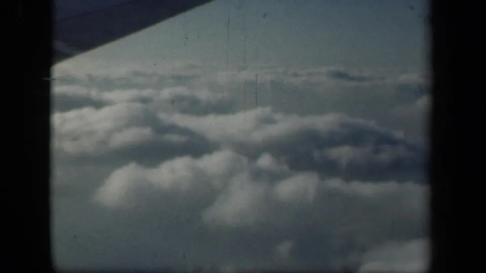 1941 8mm home-movie frame showing clouds from an airplane window, with the aircraft wing corner and dark frame edges visible.