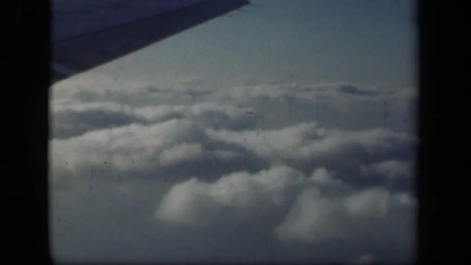 1941 passenger-view frame with rolling clouds below, a wing shape at the top left, and visible 8mm film grain.
