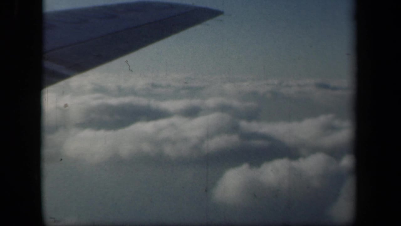 Dark aircraft wing over soft clouds with a pale sky beyond.