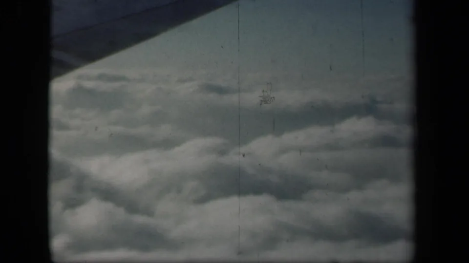 1941 8mm aerial view over layered clouds, framed by an airplane wing edge and dark film-gate borders.