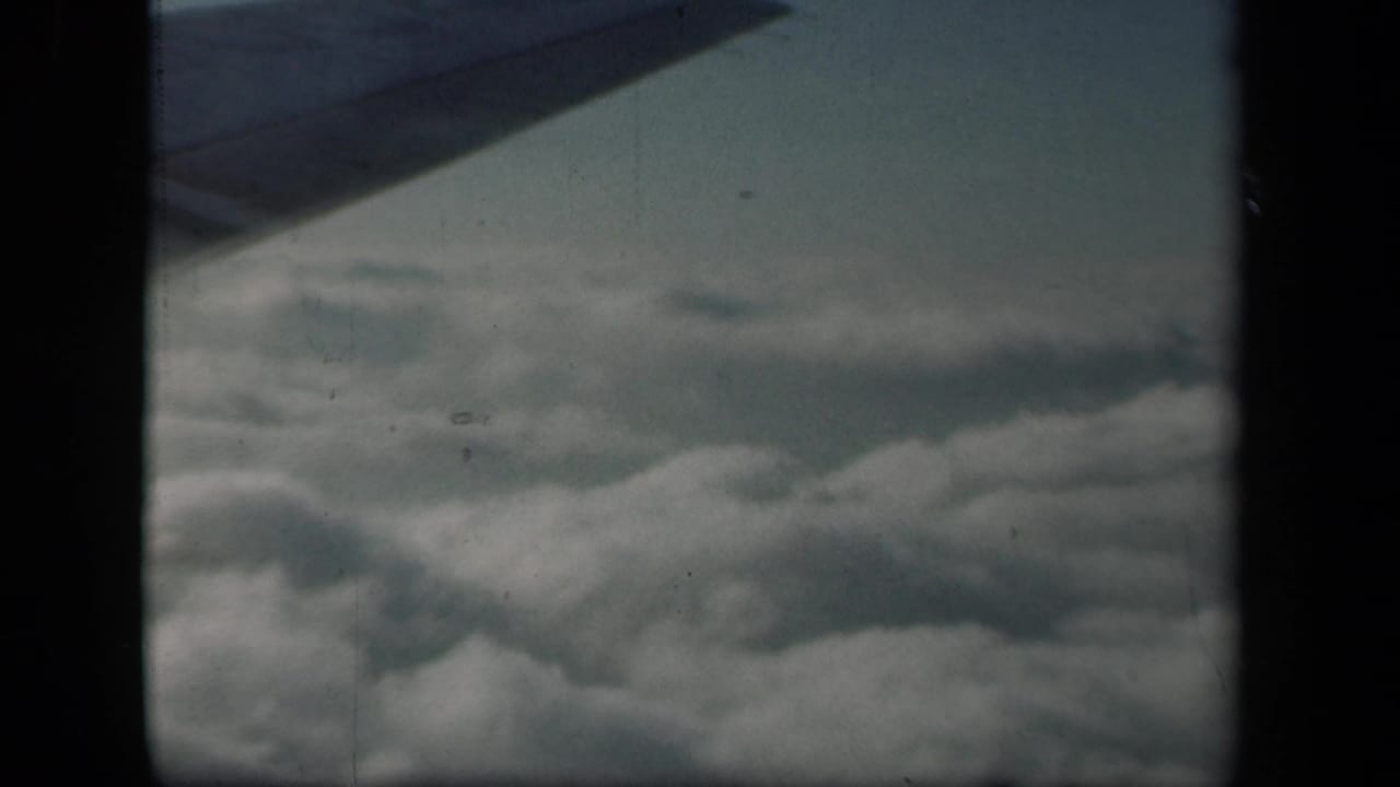 1941 8mm airplane-window view across a broad cloud bank, with the wing edge cutting across the top of the frame.