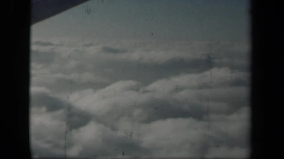 1941 8mm aerial cloudscape with muted color, heavy gate shadowing, and no identifiable ground features.