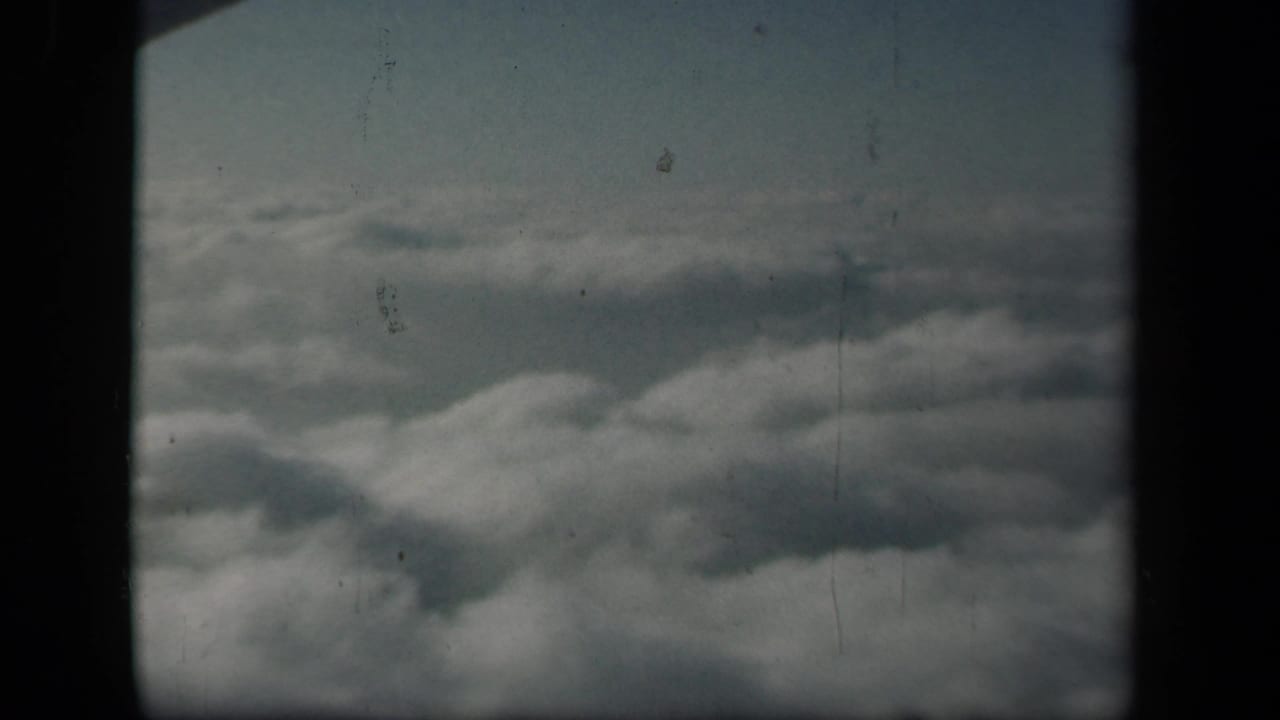 1941 8mm home-movie frame showing layered clouds through a dark airplane-window divider, with no people or landmarks visible.