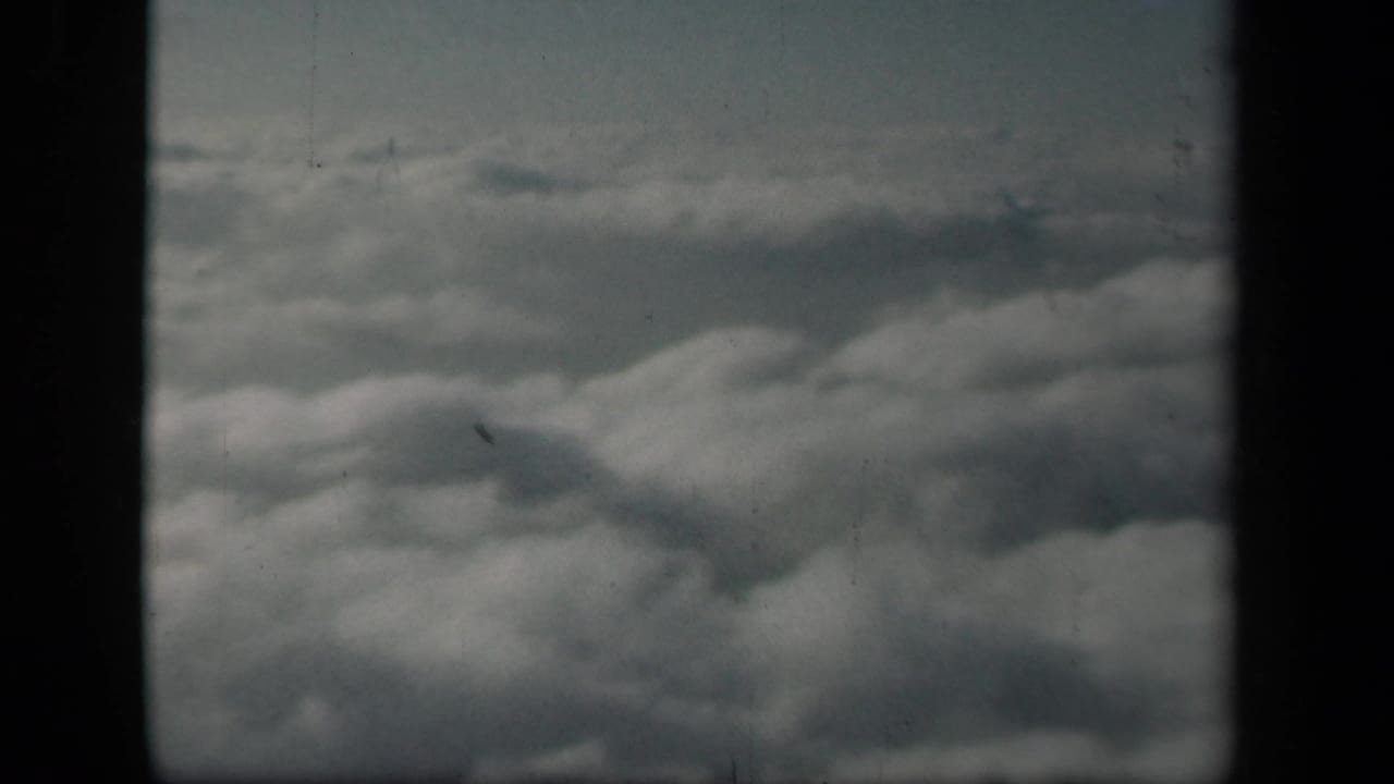 Aerial view of dense cloud tops from an airplane window in the 1941 home-movie clip, framed by dark window borders.