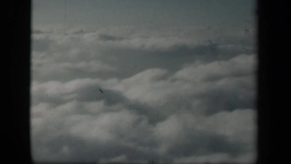 Aerial view of dense cloud tops from an airplane window in the 1941 home-movie clip, framed by dark window borders.