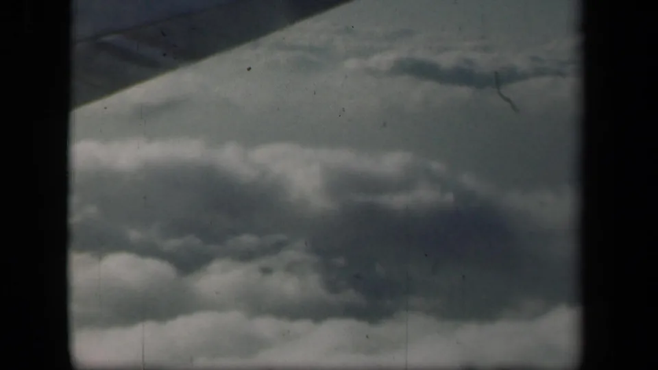 Airplane wing edge enters the frame above layered clouds in this 1941 8mm aerial travel view.
