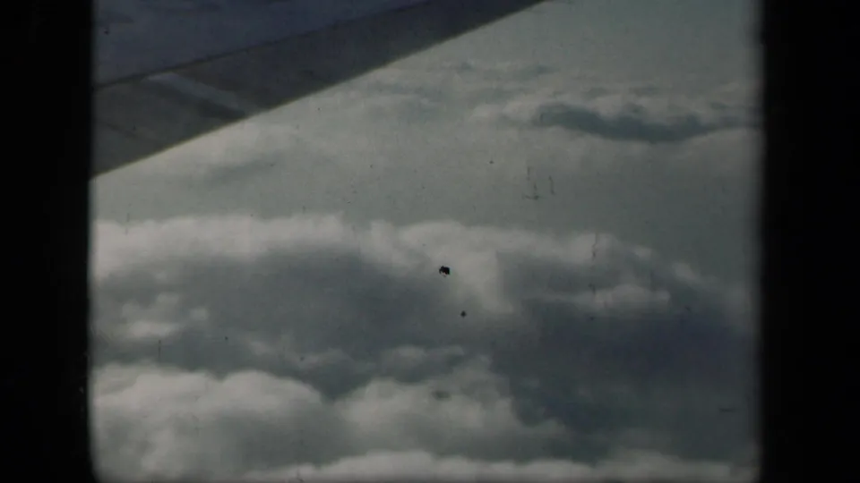1941 airplane-window view with the wing crossing above textured cloud cover, recorded on 8mm home-movie film.