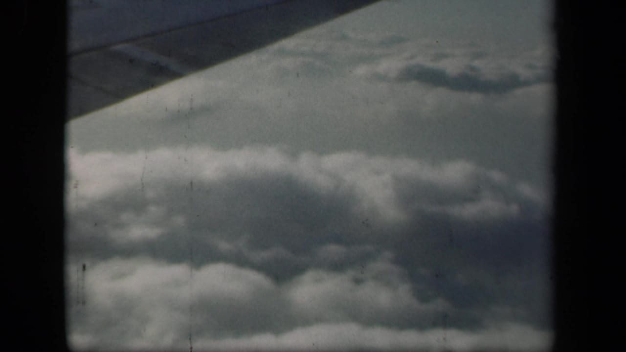 1941 8mm home-movie view from a plane, showing a wing over layered clouds near New York according to clip metadata.