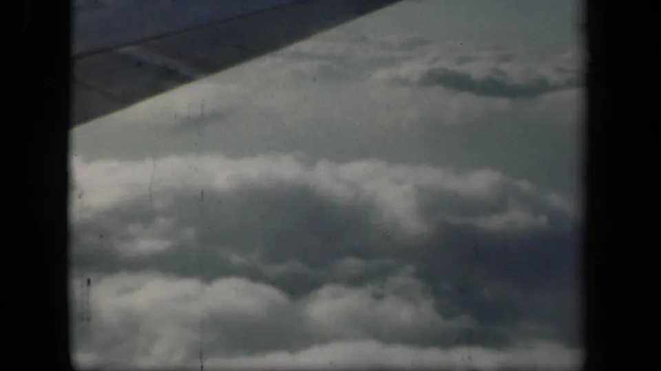 1941 8mm home-movie view from a plane, showing a wing over layered clouds near New York according to clip metadata.