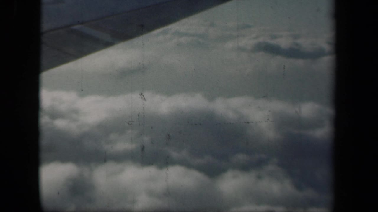Cloud banks and blue sky viewed from an airplane window, with dark frame edges.