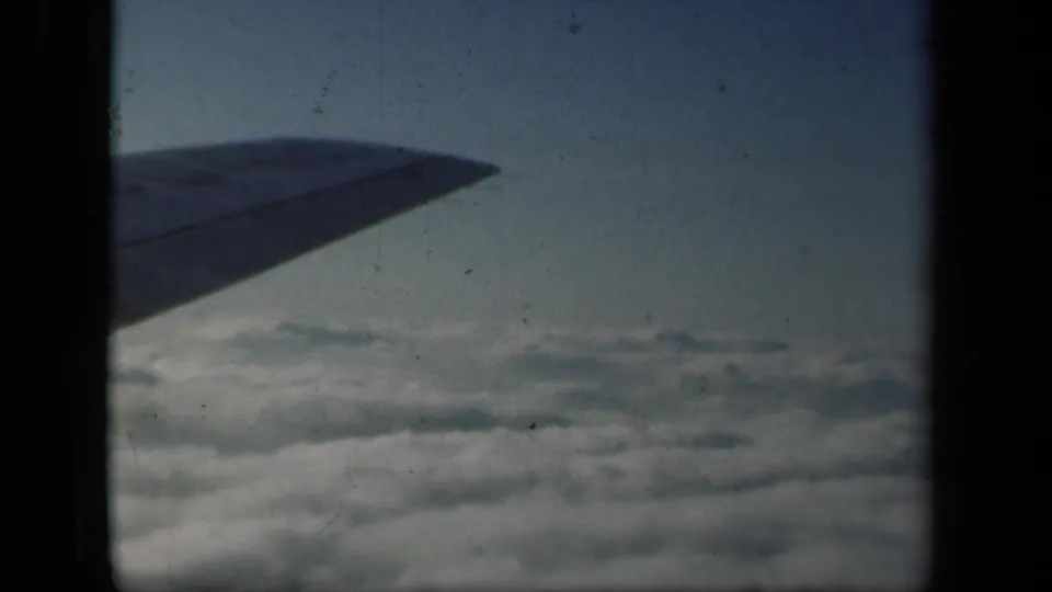 Passenger-shot 8mm frame from 1941, showing the aircraft wing over clouds with faded color and visible film wear.