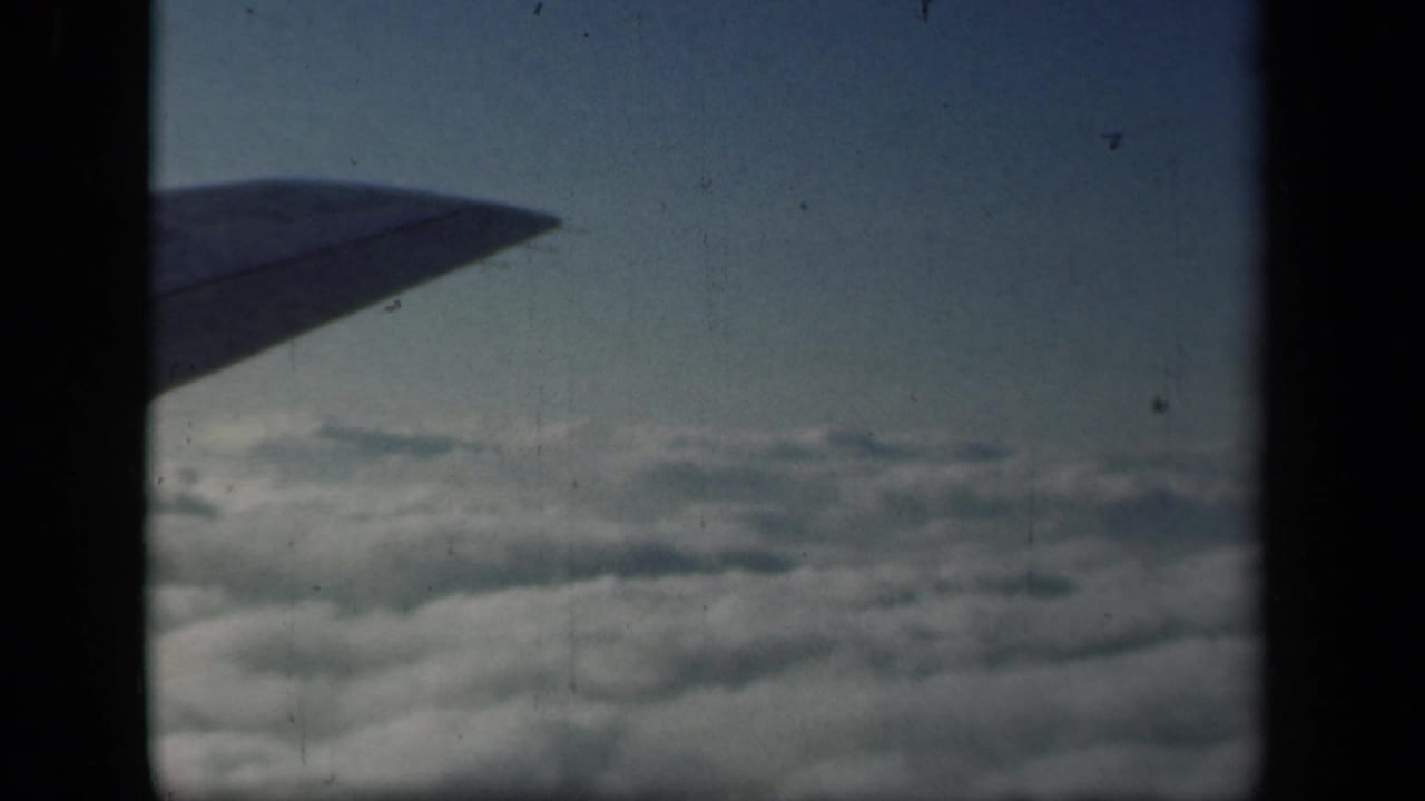 Plane wing tip extends over clouds with blue sky beyond.