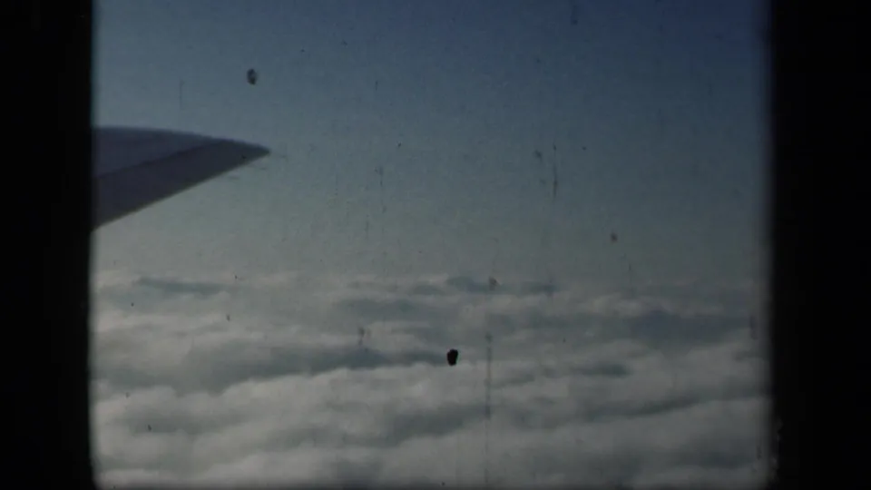 1941 passenger-window view with the aircraft wing at left, clouds below, and 8mm dust and exposure marks visible.
