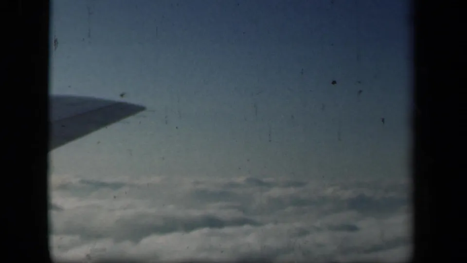 Final frame of the 8mm aerial view, with the airplane wing silhouetted against sky and clouds below.