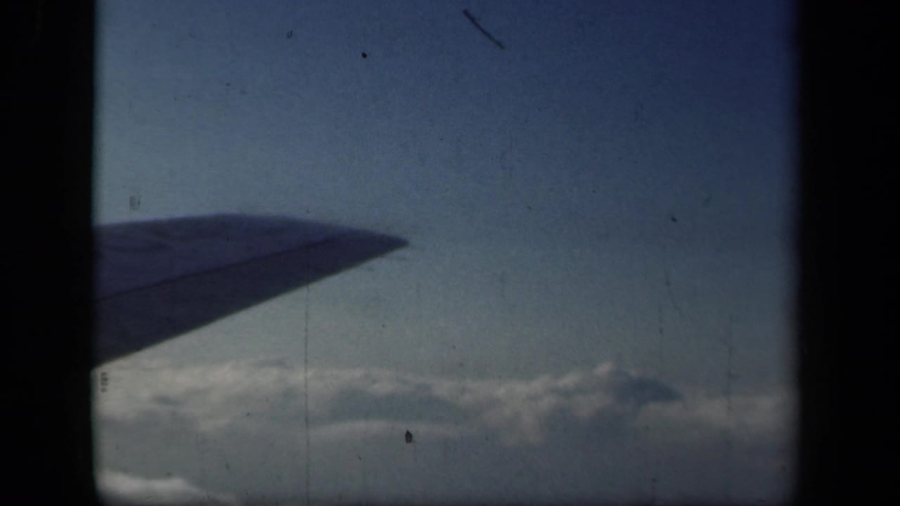 Airplane wing extends over clouds, with dark film-frame borders visible.