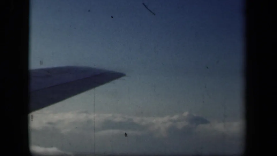1941 aerial home-movie frame showing an airplane wing above clouds, with dark window or gate edges around the view.