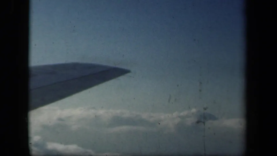 1941 8mm aerial view with a silhouetted airplane wing over a bright cloud bank and faded blue sky.